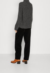 Pull-over en maille gris à col roulé avec texture côtelée, associé à un pantalon en velours côtelé noir et des bottines à talons oranges avec semelles noires.