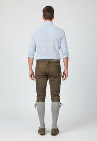 Hnědé kalhoty s texturovaným povrchem, spárované s světle modrou kostkovanou košili, šedými podkolenkami a hnědými botami.