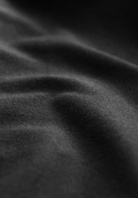 Tessuto nero con una superficie liscia e leggermente strutturata, che presenta onde e pieghe sottili, con un colore uniforme in tutto il materiale.