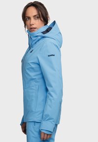 Hellblaue wasserdichte Jacke mit Kapuze, verstellbaren Bündchen und mit Reißverschlüssen versehenen Taschen. Merkmale ein schlankes Design und eine weiche, glatte Textur.