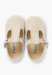 Zapatos de tela beige con una superficie texturizada, que presentan un diseño de tira en T, cierre de Velcro y detalles de hebilla plateada. Forma suave y curva.
