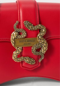 Sac à main en cuir rouge avec un fermoir à motif serpent doré et une plaque gravée "JUST CAVALLI MILANO" au centre. Texture lisse.
