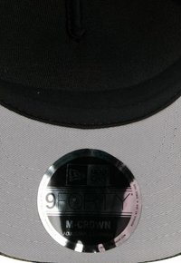 Schwarze und graue Cap mit flachem Schirm, ausgestattet mit einem runden Etikett mit den Aufschriften "9FORTY" und "M-CROWN", gefertigt aus strukturiertem Stoff.