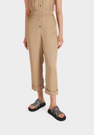 Pantaloni cropped khaki con chiusura a bottoni e due tasche laterali, abbinati a sandali grigi con zeppa dotati di una fascia testurizzata e suola nera.