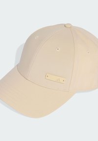 Beige čepice s pevným designem, zakřiveným okrajem a zlatou obdélníkovou accentní destičkou se znakem. Hladký povrch se šitými švy.