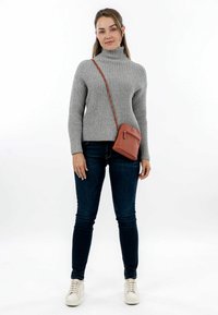 Maglione grigio a costine con collo alto, jeans slim blu scuro, sneaker bianche e una piccola borsa a tracolla marrone con tasca con zip.