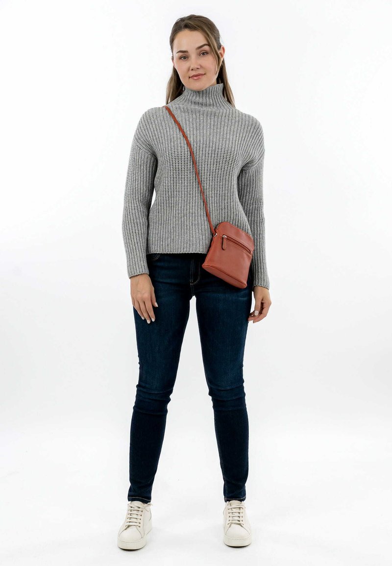 Maglione grigio a costine con collo alto, jeans slim blu scuro, sneaker bianche e una piccola borsa a tracolla marrone con tasca con zip.