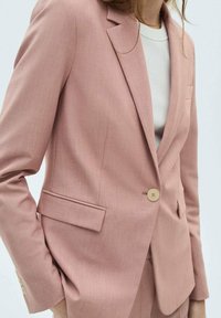 Blazer rose clair avec une fermeture à un bouton, des revers crantés et des poches latérales. Fabriqué à partir d'un tissu texturé, coupe ajustée.