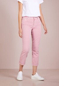Jeans in denim rosa chiaro con vestibilità slim e lunghezza cropped, dotati di chiusura a bottone e design standard a cinque tasche, abbinati a sneakers bianche.