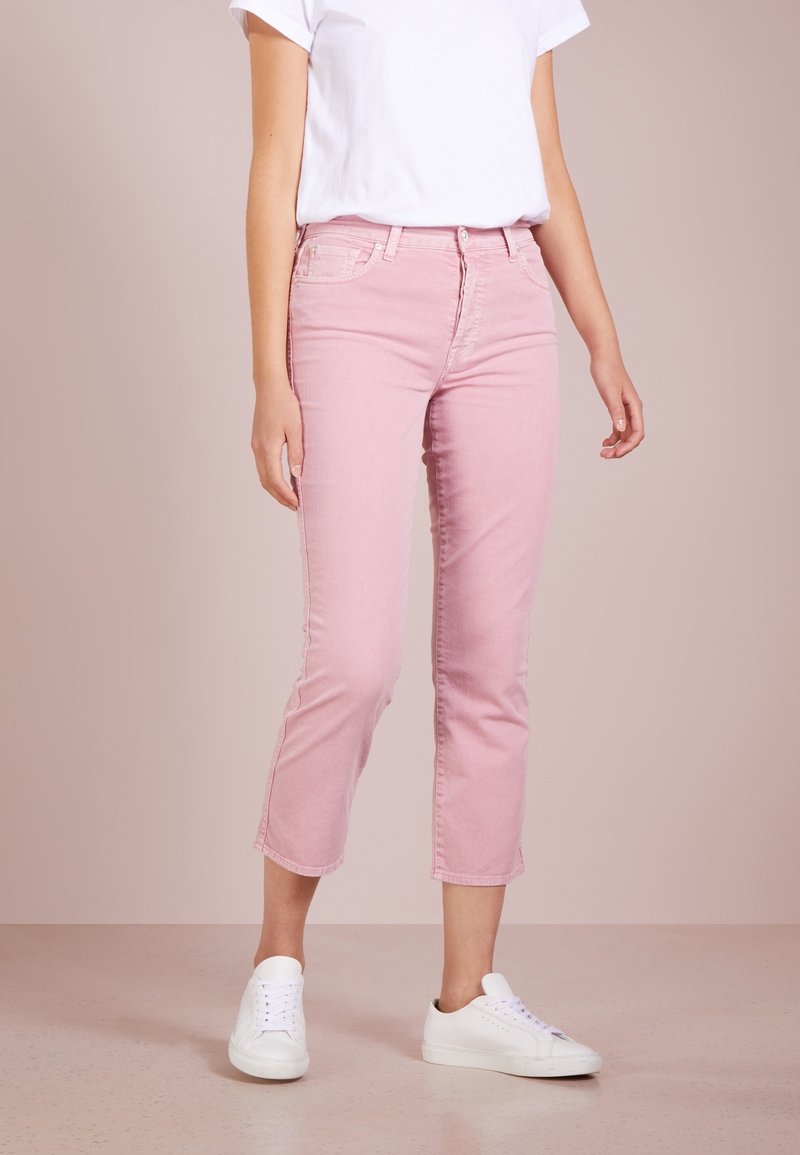 Jeans in denim rosa chiaro con vestibilità slim e lunghezza cropped, dotati di chiusura a bottone e design standard a cinque tasche, abbinati a sneakers bianche.