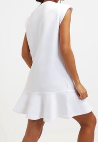 Vit ärmlös klänning med utsvängd nederkant, slät textur och minimalistisk design. Har rena linjer och rund halsringning.
