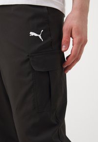 Sorte cargo bukser med slim fit, udstyret med en sidelomme og et hvidt Puma-logo på venstre ben. Glat tekstur og slidstærkt materiale.
