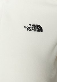 Biały polarowy pulower z czarnym, wyszywanym logo "The North Face". Gładka faktura i prosty design z okrągłym dekoltem.