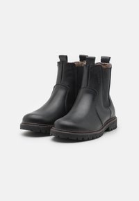 Botas de tobillo de cuero negro con paneles laterales elásticos, una suela de goma texturizada y un interior suave y acolchado.