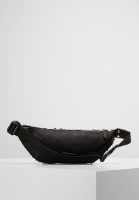 Borsa a vita nera in pelle con tracolla regolabile e cerniera, caratterizzata da piccoli chiodini decorativi lungo i bordi, esposta su un piedistallo bianco.