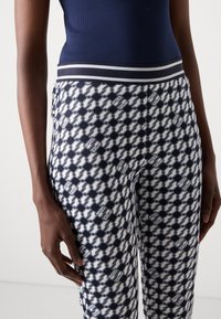 Marineblauwe en witte legging met een passend ontwerp, voorzien van een brede elastische tailleband en een herhalend logo-patroon over de gehele lengte.