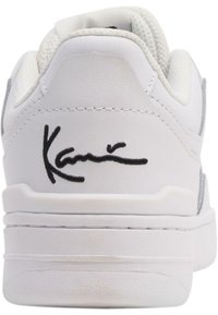 Hvide sneakers med syntetisk overdel, polstret krave og grå accents på hælen. Har sort signatur på bagsiden. Tykk hvid sål.