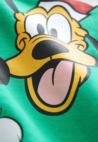 Visage de chien de dessin animé avec de grands yeux, bouche ouverte et langue pendante sur un fond de tissu vert.