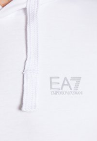 Bílá mikina s kapucí s pleteným šňůrkou, na přední straně stříbrné logo „EA7 EMPORIO ARMANI“. Hladká textura, ležérní design.