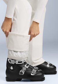 Fekete síbakancs ezüst csatokkali, fehér nadrággal, amelyen összehúzott, rugalmas boka mandzsetta található. Sima felületek és strapabíró anyagok.