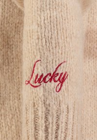 Cremfarbener Strickpullover mit gerippter Textur, auf dem Vorderteil in roser Kursive "Lucky" gestickt. Weiches Material und legeres Design.
