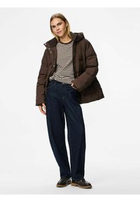 Brūns pūkains jaka ar kapuci virs melnbaltas svītrainas krekla, kopā ar brīvām tumšām denima biksēm un melnām masīvām kurpēm.