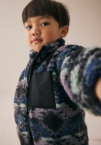 Veste en polaire aux motifs abstraits en violet, bleu et vert ; dotée d'une poche noire, d'un col montant et d'un zip complet. Matériau doux et texturé.