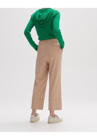 Beżowe spodnie o szerokich nogawkach w dopasowanym kroju, z mankietami i tylnymi kieszeniami, w połączeniu z zielonym swetrem z kapturem.