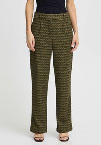 Pantalons à carreaux verts avec une coupe décontractée, en tissu texturé, taille mi-haute et plis à l'avant, associés à un haut noir et des sandales.