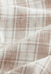 Tissu tissé brun clair et blanc avec un motif à carreaux texturé et des détails de tissage visibles.