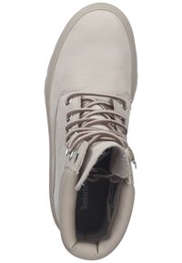 Jasnobeżowe sznurowane botki z grubą podeszwą, wyściełanym kołnierzem, metalowymi oczkami i widocznym logo Timberland wewnątrz.