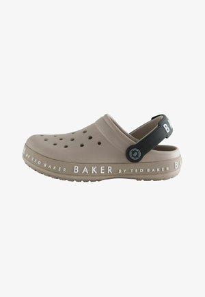Light brown slip-on clog with ventilation holes, black adjustable heel strap, and "Baker by Ted Baker" branding on sole and strap.