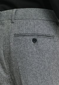 Gewebter grau-weißer Fischgrätenmuster-Stoff von Hosen mit einem schwarzen Knopf, einer Gesäßtasche und einem flachen Vorderdesign.