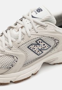 Helle beige Laufsohle aus Mesh-Material, mit Gummisohle und einem navyblauen Logo. Die Schnürsenkel und die Dämpfung tragen zur praktischen Gestaltung bei.