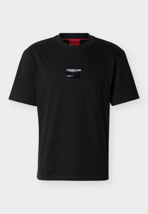 T-shirt noir à manches courtes avec un petit patch logo carré noir brillant centré sur la poitrine et une étiquette de col intérieure rouge.