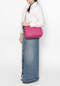 Roze leren schoudertas met een gladde textuur, rechthoekige vorm en een frontknopdetail. Gekomd met een witte shirt en denim rok.