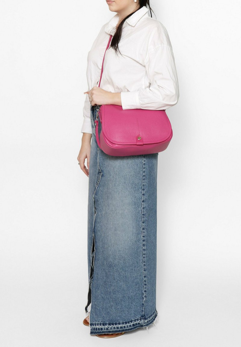 Roze leren schoudertas met een gladde textuur, rechthoekige vorm en een frontknopdetail. Gekomd met een witte shirt en denim rok.