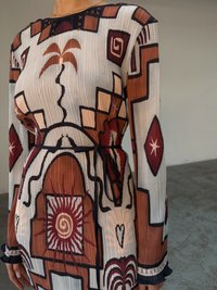Robe texturée avec un motif rayé en crème, rouille et bordeaux. Présente des motifs géométriques, une taille à nouer et des manches longues.