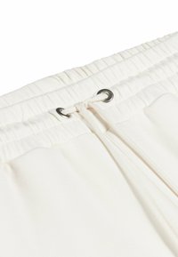 White sweatpants featuring a gathered elastic waistband, drawstring with silver eyelets, and soft textured fabric.