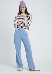 Pull en rayures avec des lignes roses, bleues et marine ; pantalon large bleu clair ; bonnet en tricot violet ; baskets blanches avec des semelles claires.
