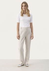 Pantaloni beige in tessuto texture, taglio dritto, con tasche anteriori e vita alta. Abbinati a un top aderente bianco a maniche corte.