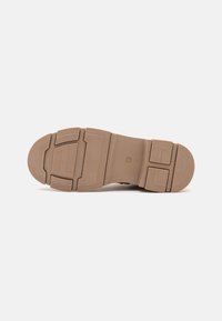 Light brown sneaker sole with a textured pattern, featuring molded sections for grip and reinforcement, flat and slightly raised in design.