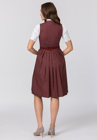 Bordeauxfarbene A-Linien-Kleid aus gemustertem Stoff, mit einem satinartigen Taillenbund und Falten. Kombiniert mit einer weißen Bluse und grauen High Heels.