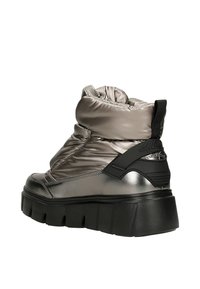 Srebrne ocieplane botki za kostkę z grubą czarną podeszwą i czarnym paskiem na pięcie, zaprojektowane do noszenia zimą i zapewniające lepszą przyczepność.