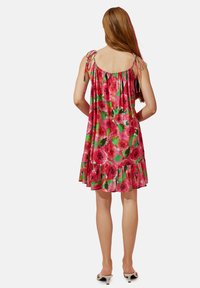 Vestido floral en rosa y rojo con un dobladillo con volantes, hecho de tela ligera. Cuenta con tirantes tipo espagueti con detalles ajustables de lazo.
