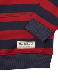 Röd och marinblå randig sweatshirt med ribbade manschetter och nederkant, med en vävd etikett som säger "Band of Rascals." Tillverkad av ekologisk bomull.