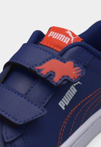 Μπλε αθλητικό παπούτσι Puma με πορτοκαλί ραφές, ιμάντα Velcro με διακοσμητικό πατς κόκκινου ρινόκερου και κόκκινο λογότυπο Puma στη γλώσσα.