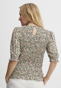 Blomsterbluse i let stof med smockdesign, pufærmer og en nøglehulldetalje bagpå. Farverne inkluderer pink, grøn og creme.