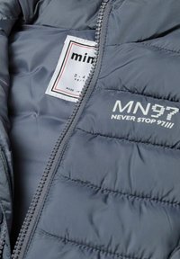 Graue Daunenjacke mit gestepptem Innenfutter, featuring ein weißes Logo "MN97 NEVER STOP 97" und Etikett. Reißverschlussdetail entlang des Randes.