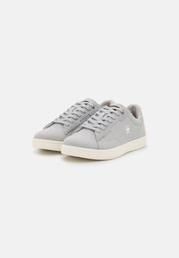 Grey canvas sneakers with a textured surface, white rubber soles, and round laces. Features subtle branding on the side and tongue.